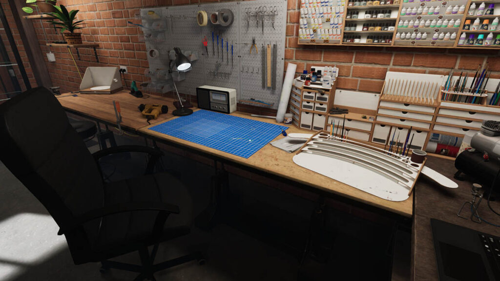 Screen z gry Model Builder przedsawia warsztat osoby zajmującej się pracą z modelami. Na biurku znajdują się akcesoria do budowania modeli, obok biurka stoi puste czarne krzesło. Na ścianach wiszą farbki i pędzle.